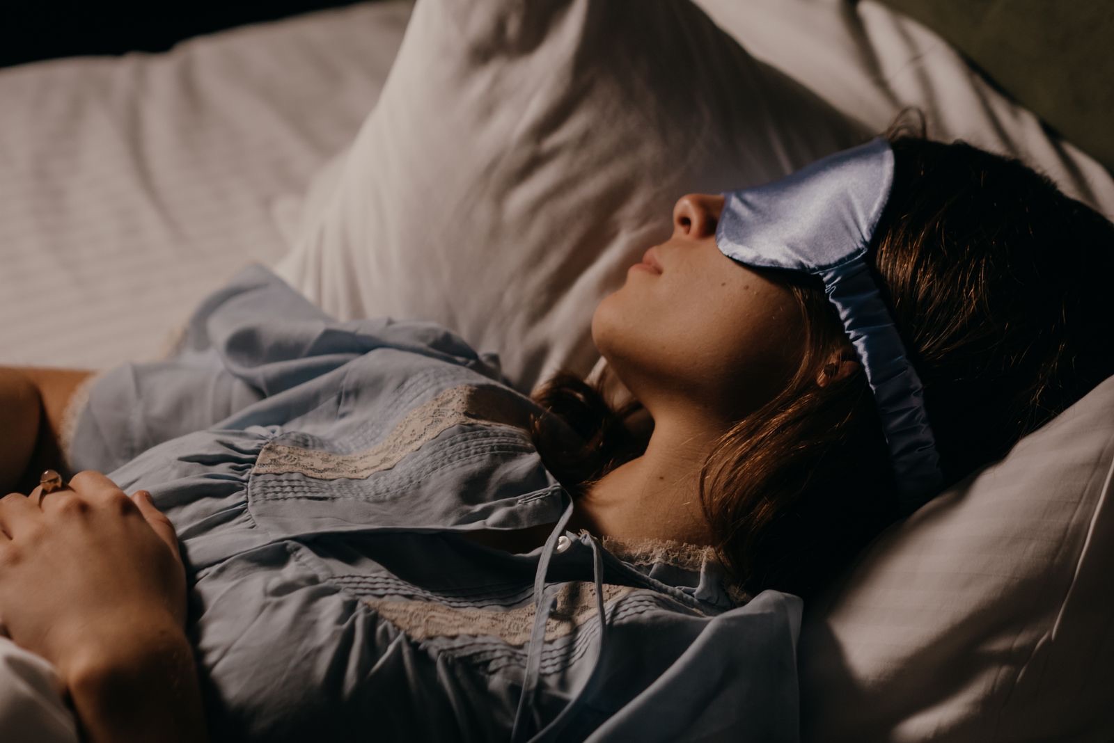 Kvinna sover på rygg i sängen med en ljusblå sovmask över ögonen.