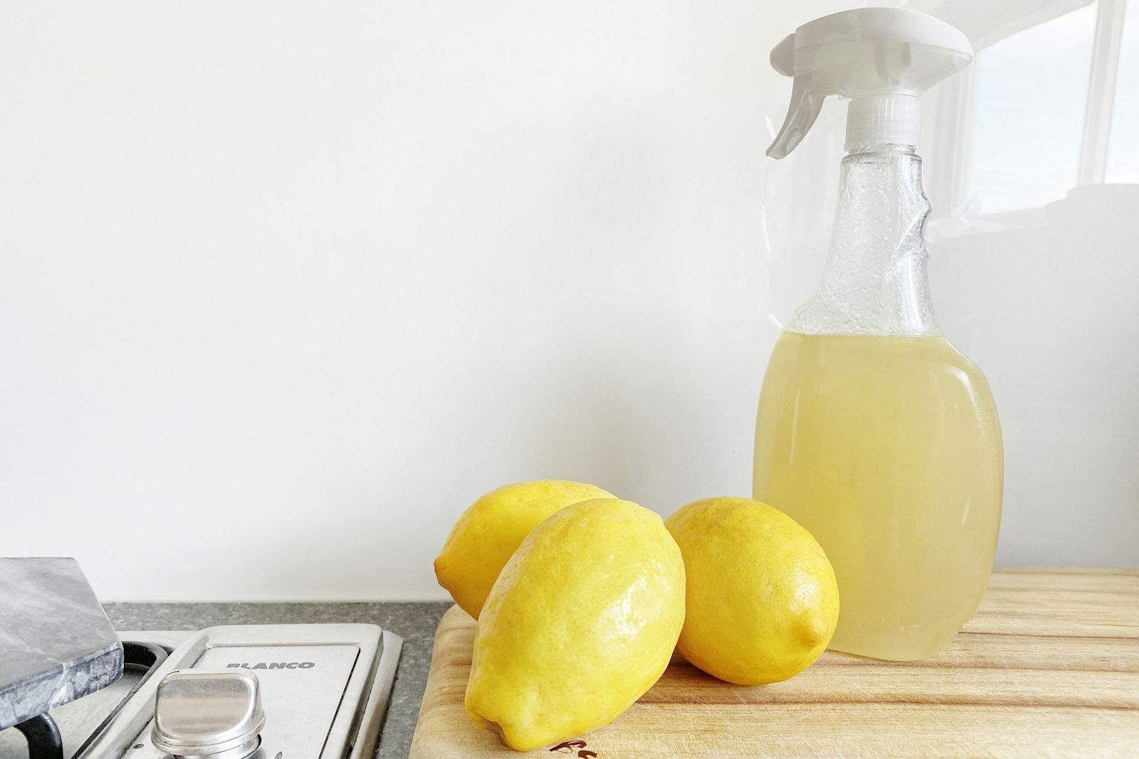 Sprayflaska med hemmablandat rengöringsmedel bredvid tre citroner på en skärbräda i köket